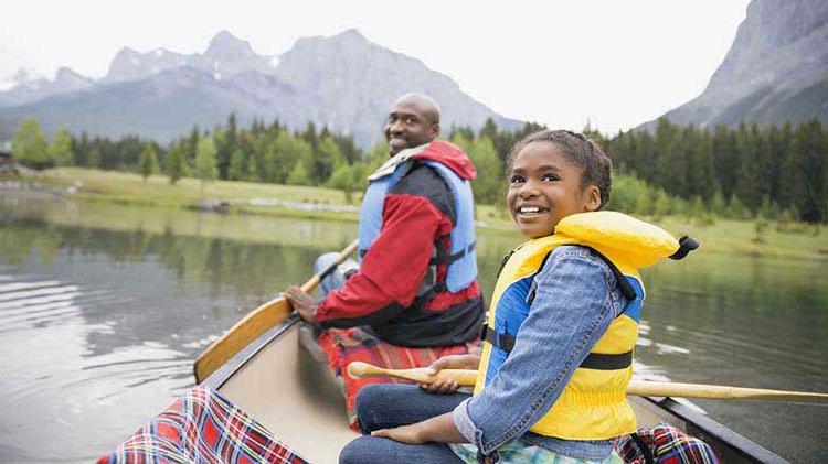 Father and daughter wearing paddle life jackets in a canoe.