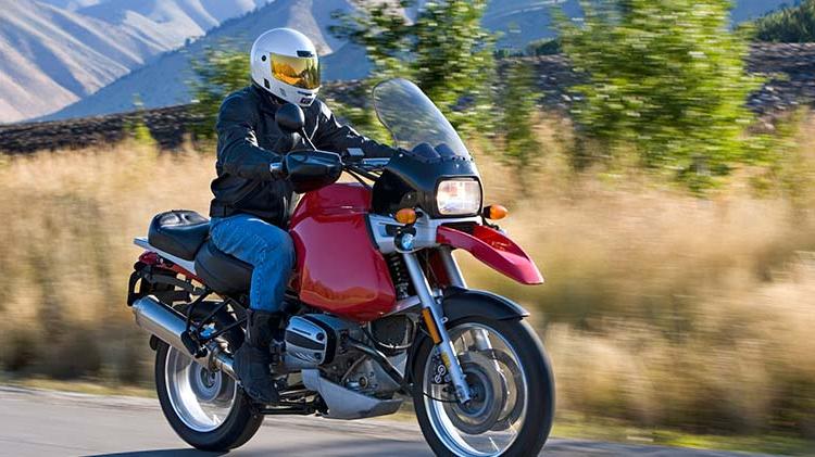 Man riding a red motorcycle with hills in the background.