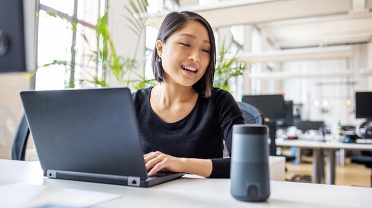 Young woman interacting with a digital voice assistant while working on her laptop.