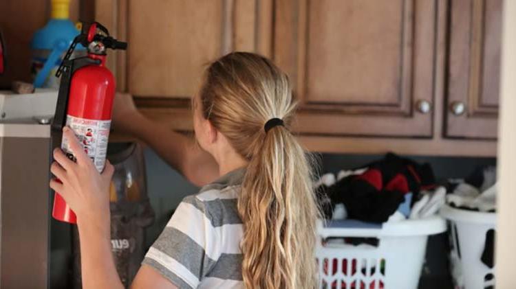 Girl putting fire extinguisher in laundry cabinet.