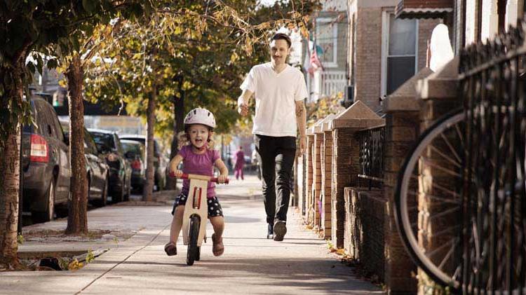 Father watching his young child ride a bike and considering the importance of life insurance.