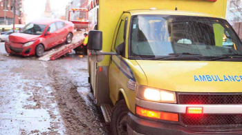 A yellow ambulance parks near a damaged white vehicle.